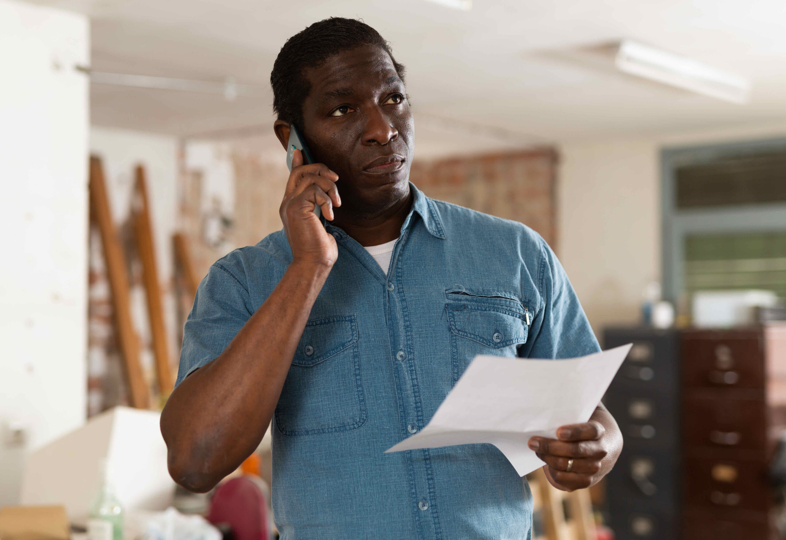 Puzzled african american with papers talking on phone during home renovation
